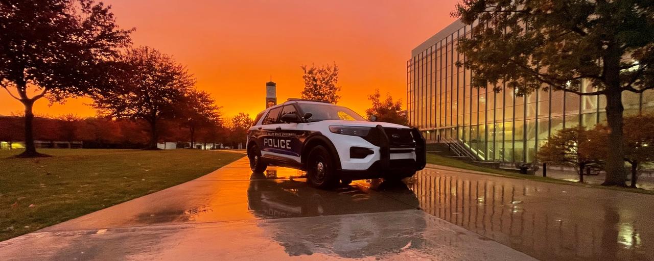 Police cruiser with sunset as background in front of clock tower and library on a rainy day